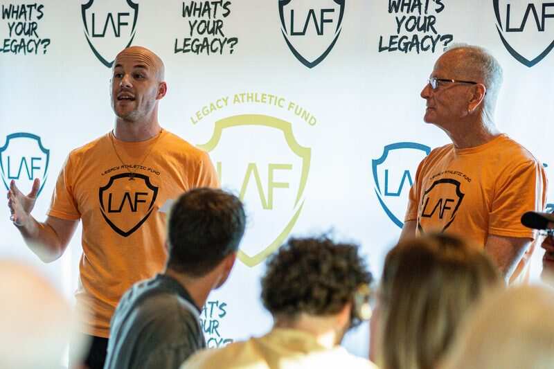 LAF leadership addressing the crowd at Trivia Night with Legacy Athletic Fund backdrop
